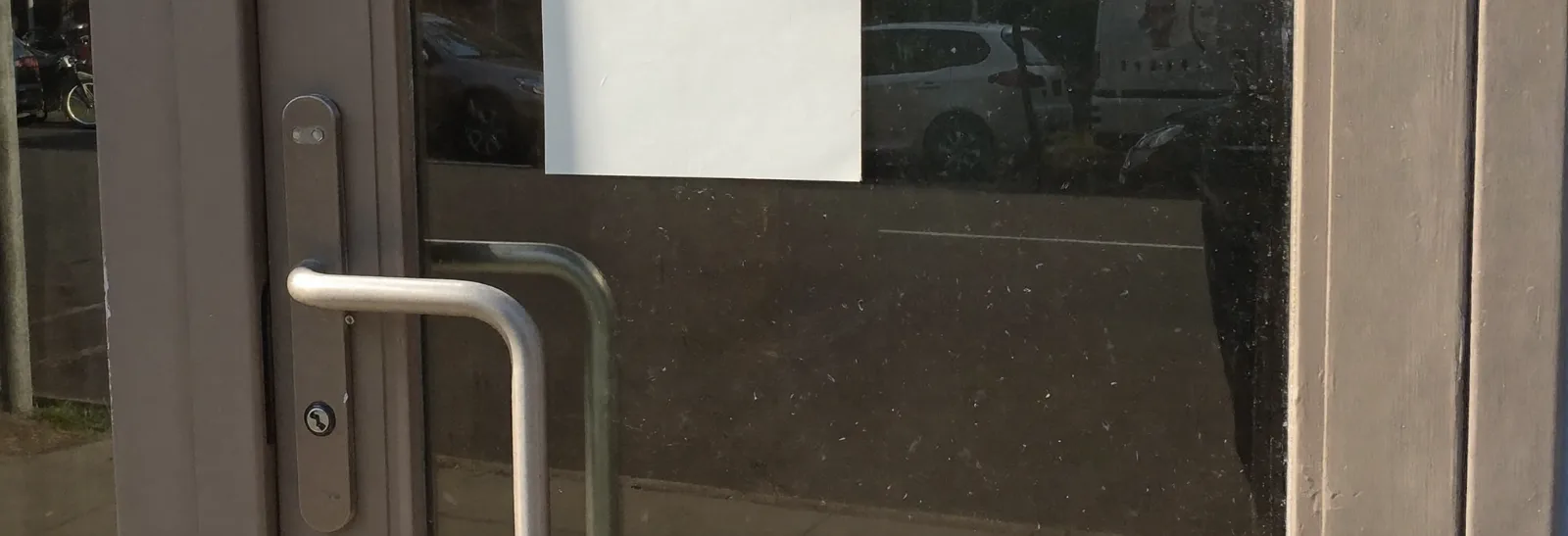 The glass door of a closed shop, with a blank white card taped inside where the opening hours would normally be.